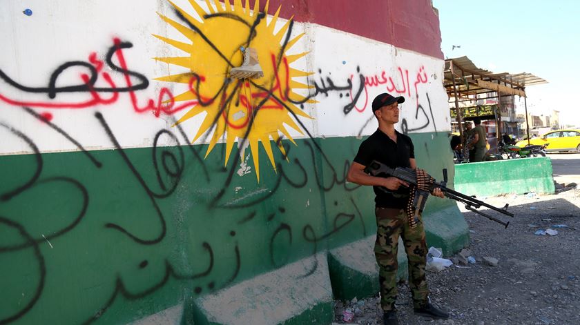 Miliciano xiita leal a Bagdad em Kirkuk frente a um mural com uma bandeira do Curdistão vandalizado. Foto: Barreq al-Samarrai/EPA