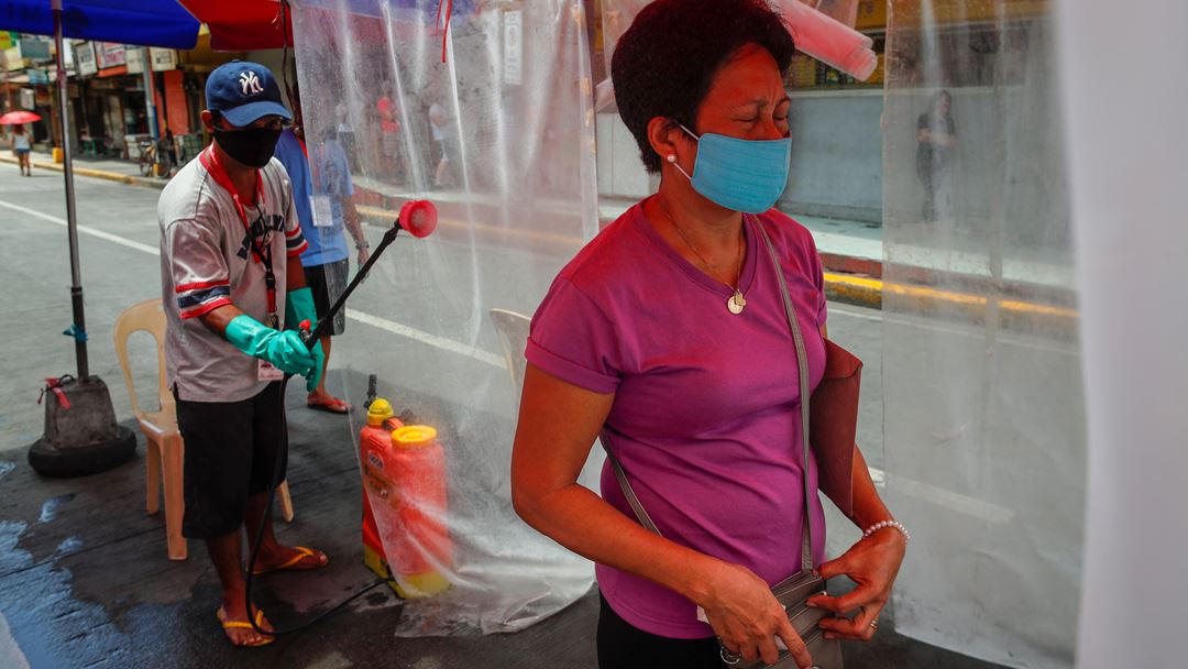 Manila, Filipinas. Uma mulher é pulverizada com desinfetante, à entrada de um mercado público. Foto: Mark R. Cristino/EPA