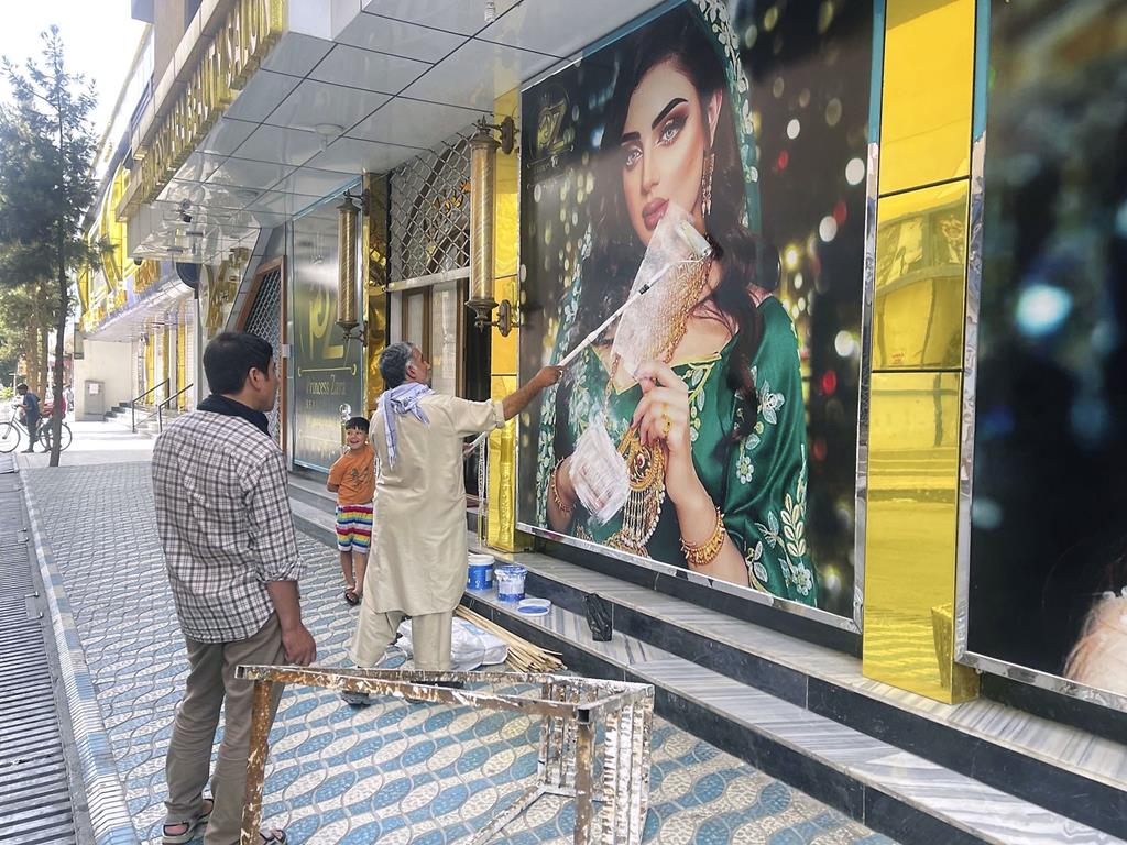 Um trabalhador de um salão de beleza pinta sobre uma fotografia de uma mulher numa parede em Cabul, a 15 de Agosto de 2021, na sequência da notícia de que os talibãs invadiram a capital afegã.