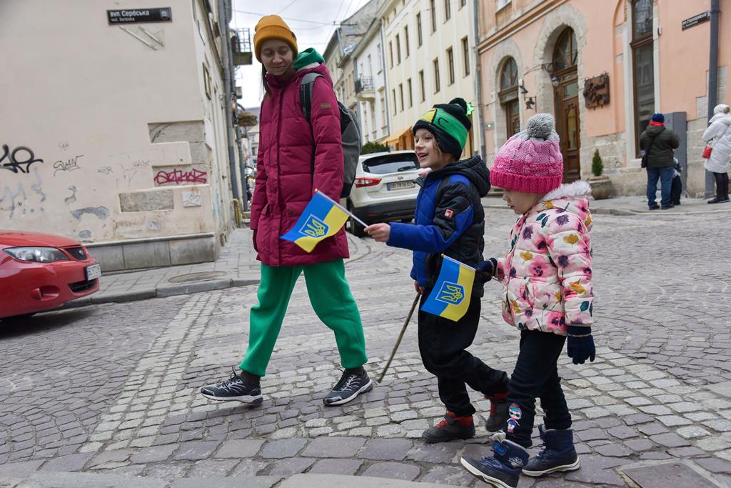 Mulher passeia com os dois filhos, que trazem bandeiras da Ucrânia. Foto: Vitaly Hrabar/EPA