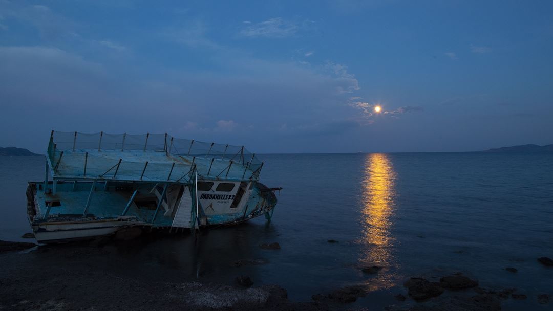 O que resta de um barco de migrantes iluminado pelo eclipse em Sivrice, Turquia, na costa do Mar Egeu. Foto: Tolga Bozoglu/EPA