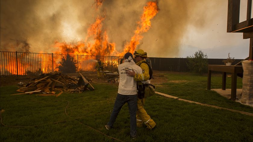 Bombeiro consola homem que tenta proteger casa. Foto: David McNew/EPA