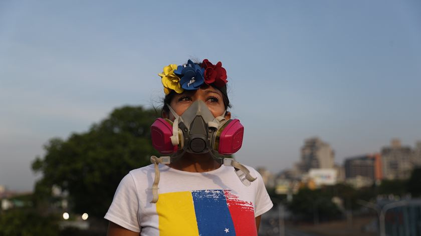 Uma simpatizante do Presidente Interino, Juan Guaidó, usa uma máscara para se proteger do gás lacrimogéneo lançado pela Guarda Nacional Bolivariana, durante os confrontos em La Carlota, no dia 30 de abril – uma pessoa acabou por ficar ferida durante os confrontos na base militar. Fotografia: Miguel Gutierrez/EPA