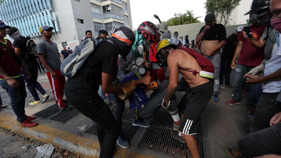 Vários manifestantes auxiliam um (dos muitos) feridos dos protestos na capital da Venezuela. Até ao momento, registaram-se mais de 130 feridos e dois mortos. Fotografia: Rayner Pena/EPA