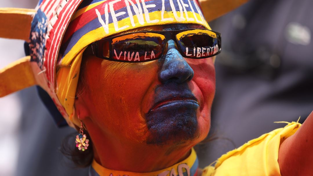 Apoiante da oposição, com a bandeira da Venezuela pintada no rosto, ouve o discurso de Juan Guaidó, no 1º de maio, em Caracas, um dia depois de os confrontos começarem. Fotografia: Miguel Gutierrez/EPA