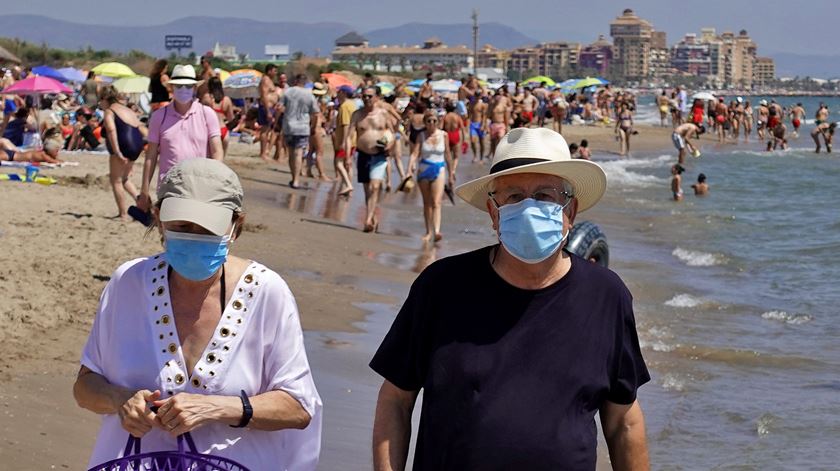 Turistas com máscaras Covid-19 numa praia de Valência, Espanha. Foto: Manuel Bruque/Lusa